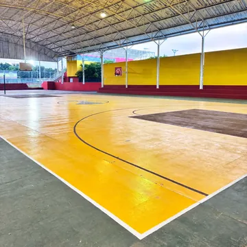 Esquina de la cancha: piso amarillo con líneas negras y blancas, gradas rojas y muro amarillo bajo el techo.