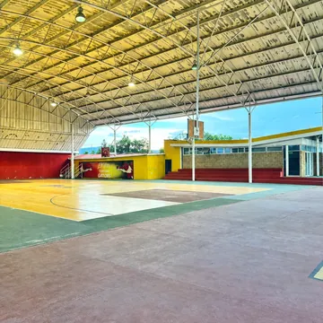 Costado de la cancha techada con el pasillo de piso rojo y las gradas al fondo.