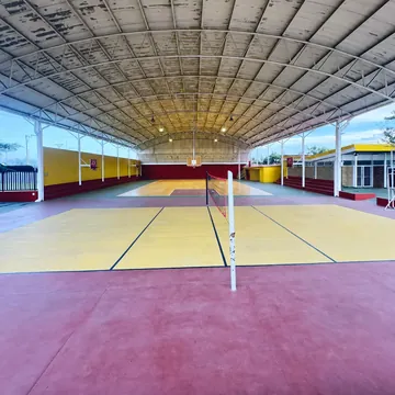 Vista a lo largo del techado: piso amarillo y rojo, una red al centro y la cancha hasta el fondo.